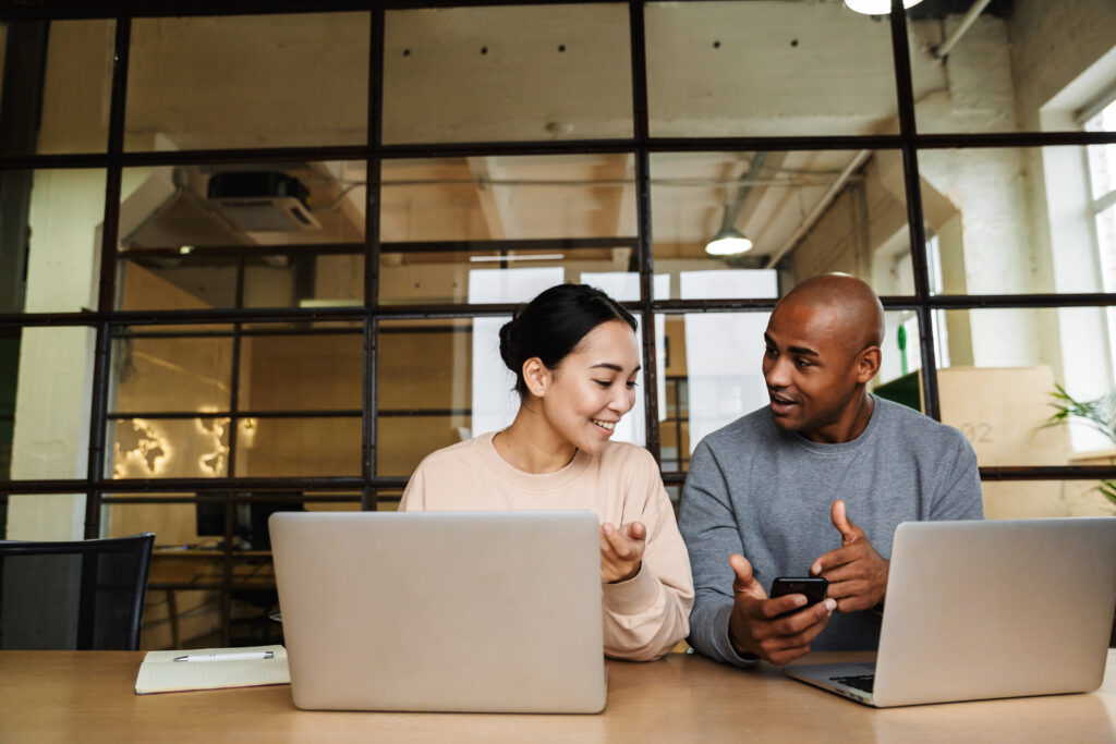 uma mulher e um homem conversam com um notebook aberto na frente de cada um